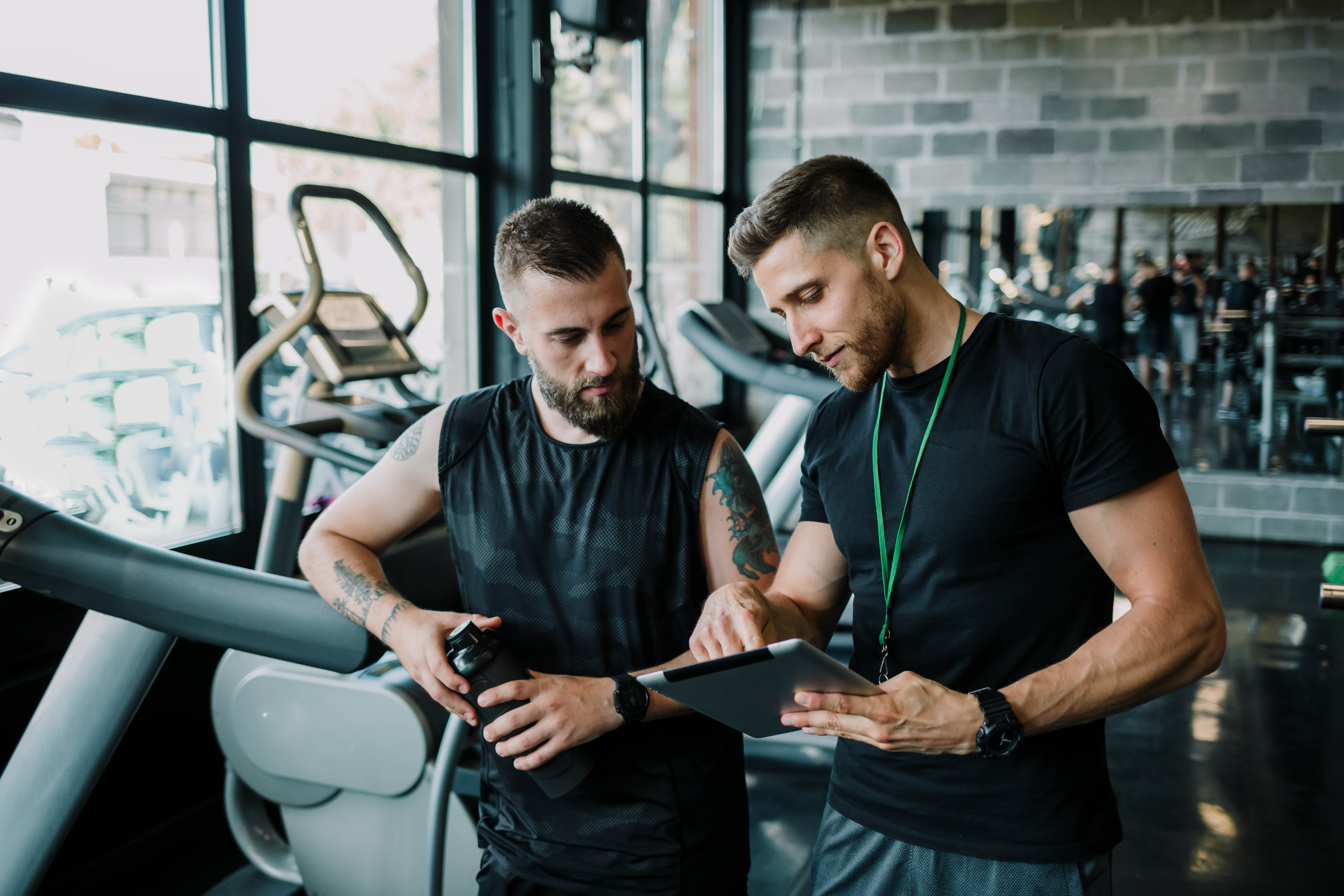 Male trainer meets with young, male client to discuss over a tablet in the gym